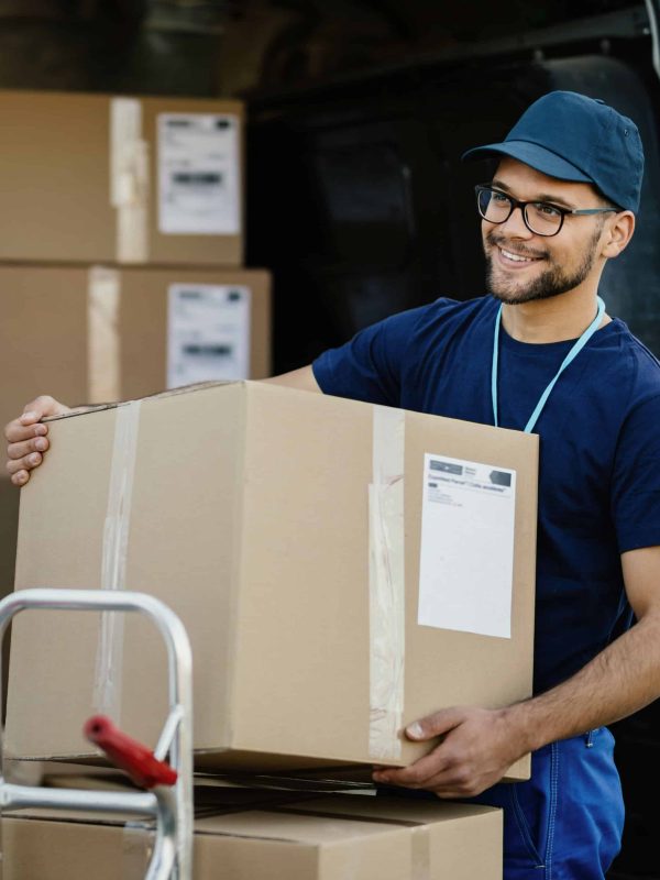 Young happy delivery man unloading boxes from a mini van and talking with his coworker.